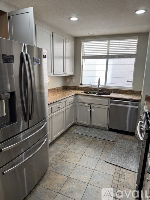 A kitchen with a stainless steel refrigerator and a window with blinds.