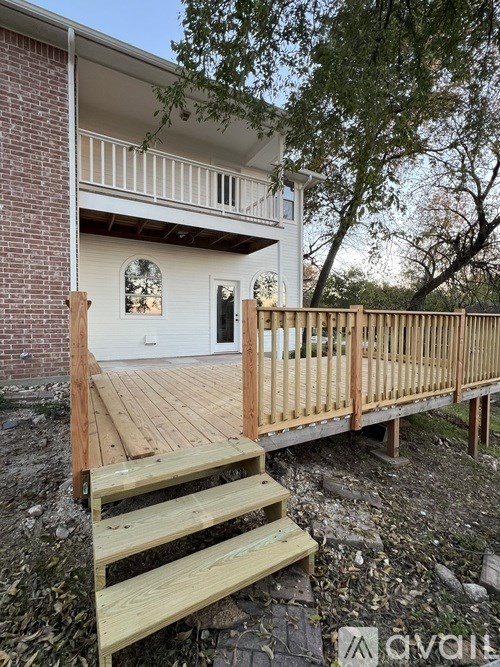 A wooden deck with steps leading to a white house with a balcony.