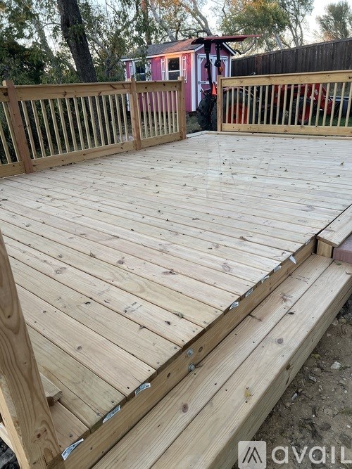 A wooden deck with a railing and a red building in the background.