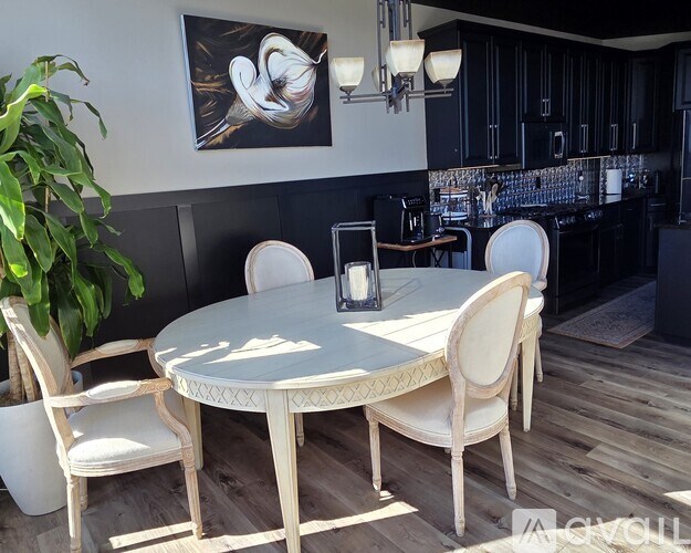 A white table with four chairs is in the foreground of a kitchen.
