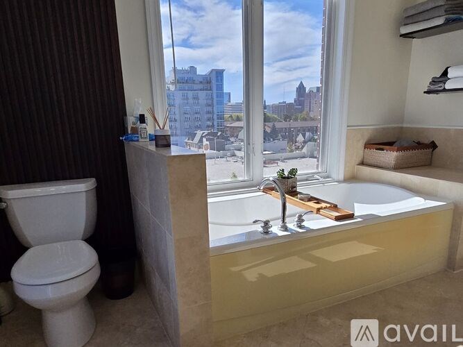 A bathroom with a toilet, a bathtub, and a window overlooking a cityscape.