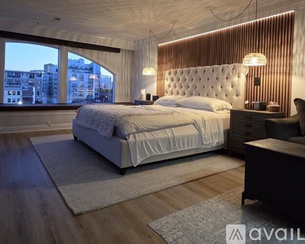 A bedroom with a large bed, a wooden headboard, and a view of the city through the window.