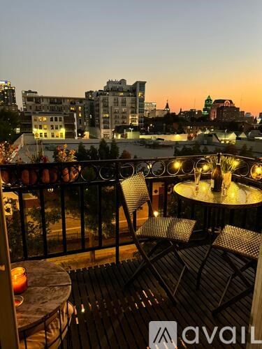 A balcony with chairs and a table overlooking a cityscape at dusk.