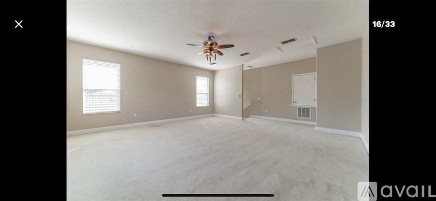 A spacious room with a ceiling fan and two windows.