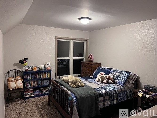 A bedroom with a bed, a chair, a window, and a bookshelf.