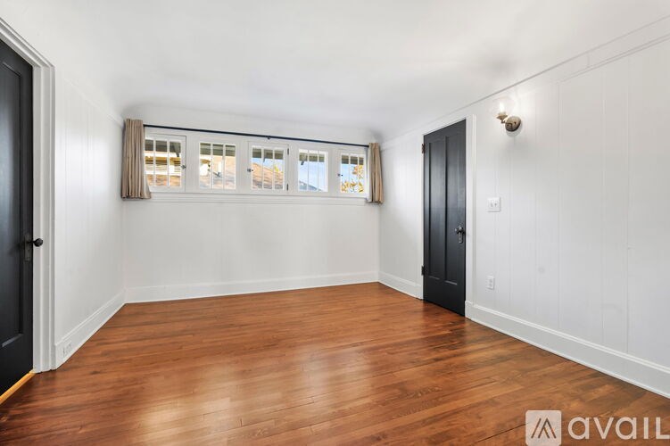 A room with wooden floors and white walls, with a window covered by a beige curtain.
