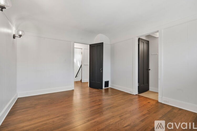 A room with wooden floors and white walls, with two black doors and a tripod in the corner.