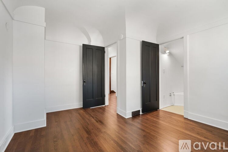 A room with wooden floors and white walls has two black doors.