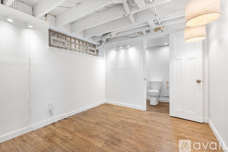 A room with wooden floors and white walls, with a toilet visible in the corner.