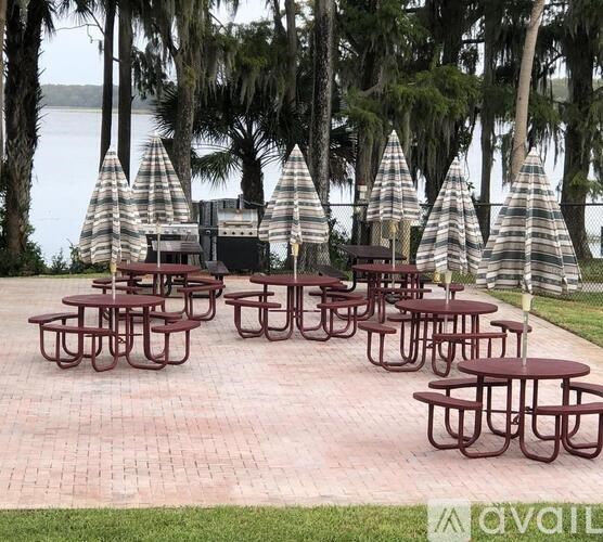 Picnic tables are set up under umbrellas by the water.