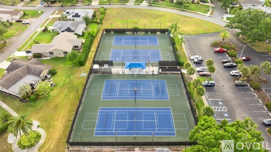 An aerial view of a tennis court surrounded by a parking lot and residential houses.