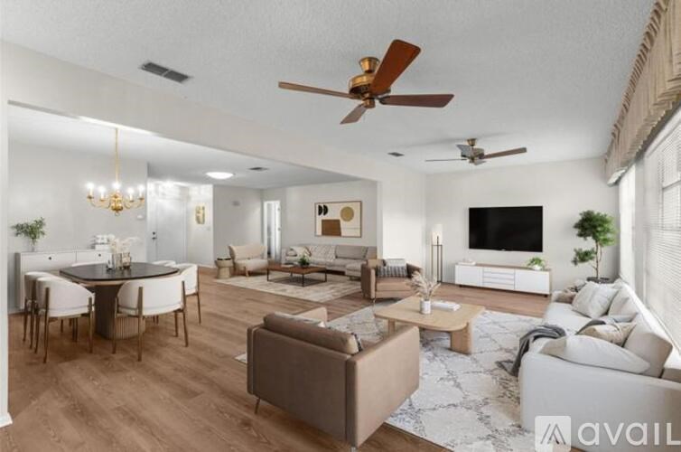 A living room with a brown sofa, a white couch, a dining table with chairs, a chandelier, and a television.