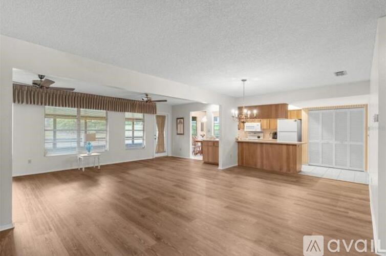A spacious living room with wooden floors and a kitchen area in the background.