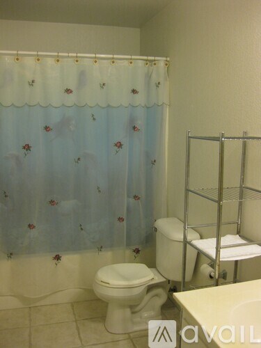 A white toilet sits under a shower curtain with a floral pattern.