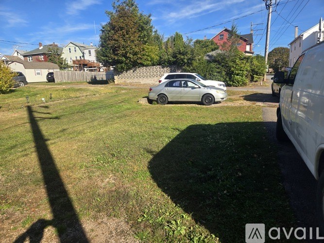A silver car is parked in a grassy area with houses in the background.
