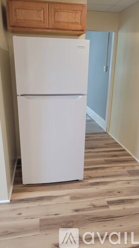 A white refrigerator in a room with wooden flooring.