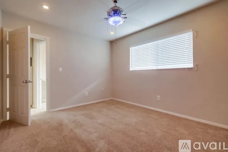 A room with a carpeted floor, a ceiling fan, and a window with blinds.