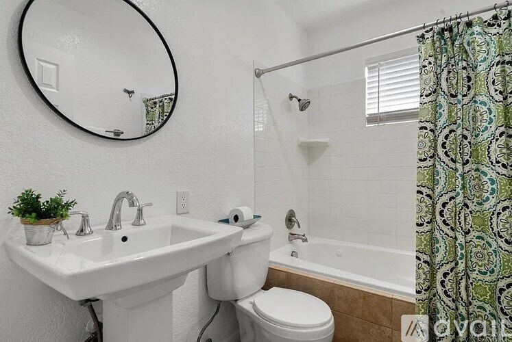 A bathroom with a white sink, toilet, and a shower with a green and white shower curtain.