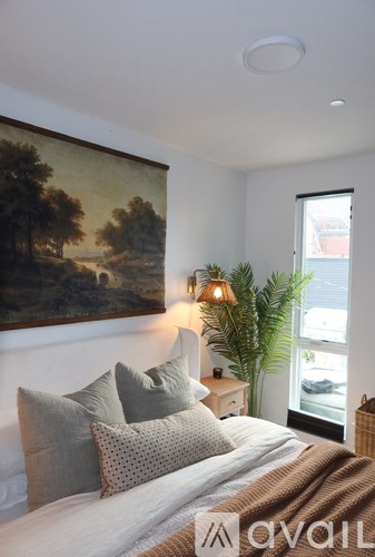 A bedroom with a large painting on the wall and a bed with pillows.