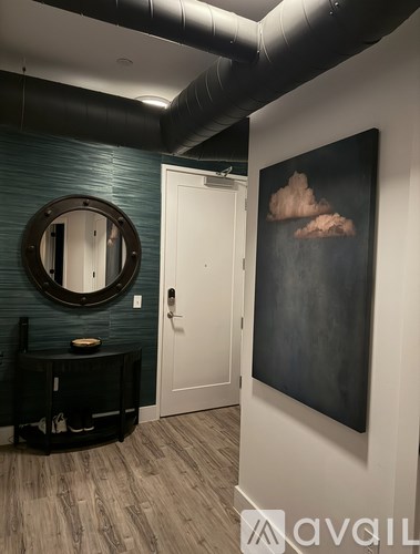 A room with a round mirror and a painting of clouds on the wall.