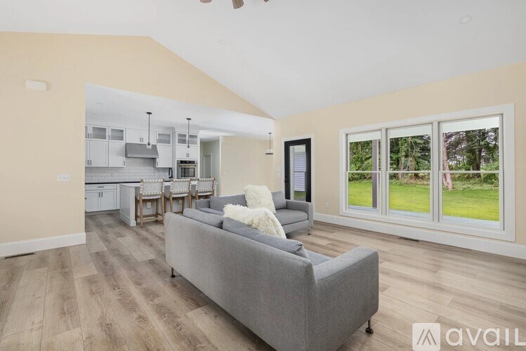 A living room with a grey couch and a kitchen in the background.