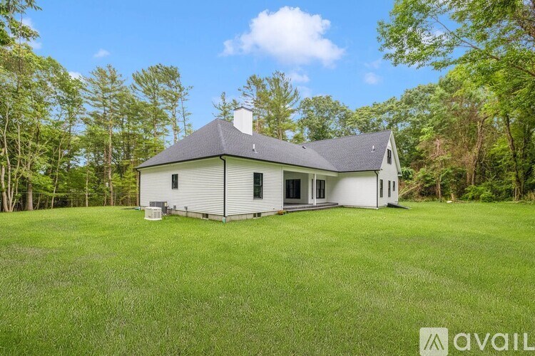 A house with a grey roof and white walls is surrounded by green grass and trees.