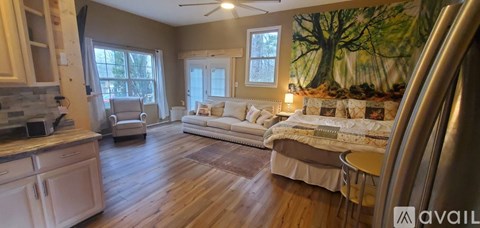 A living room with a large painting on the wall and a kitchen area to the left.