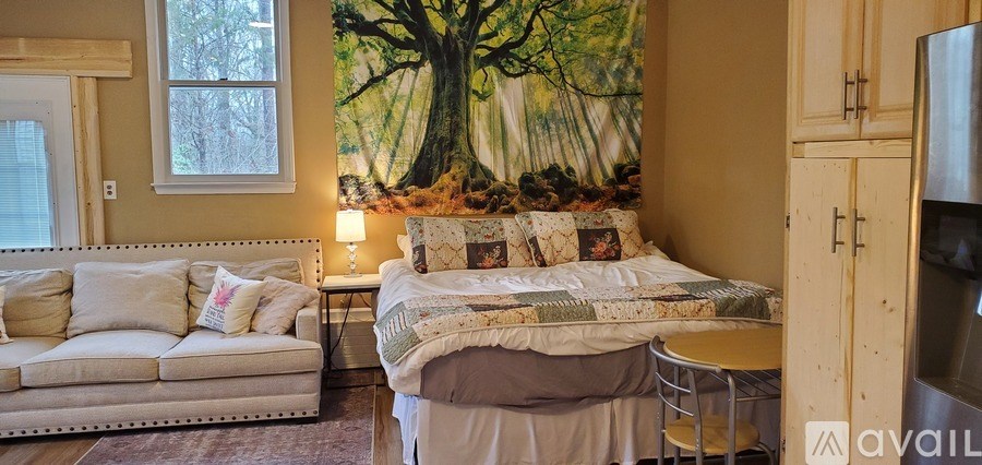 A bedroom with a bed, a couch, and a large tree mural on the wall.