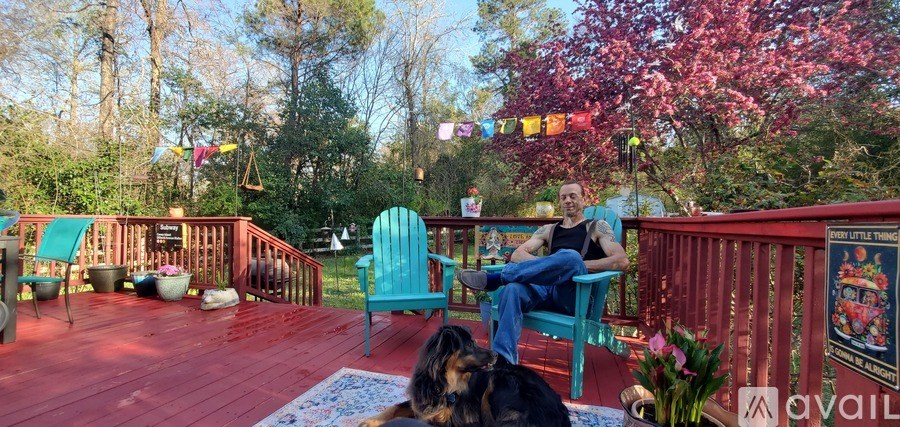 A man is sitting on a blue chair on a red deck with a dog lying in front of him.