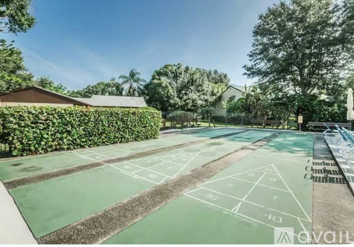A tennis court with green markings and white lines is surrounded by trees and a building.