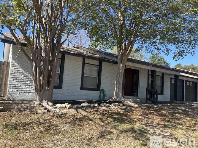 A white house with a brown roof and a tree in front.