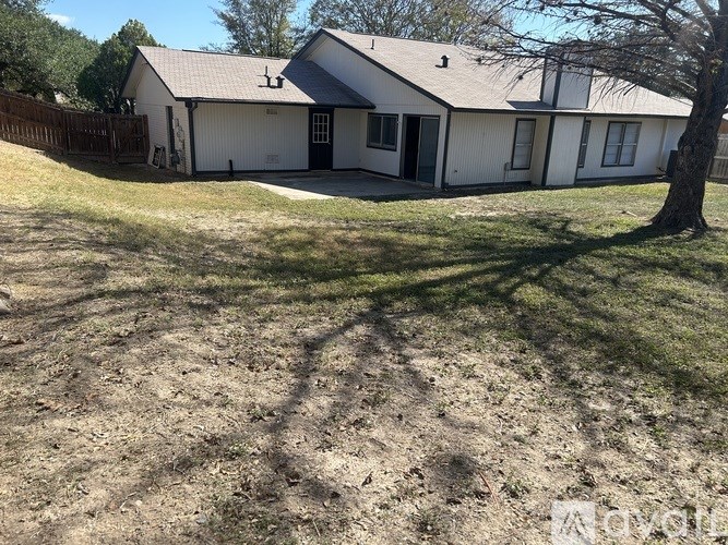 A white house with a brown roof and a tree in front.