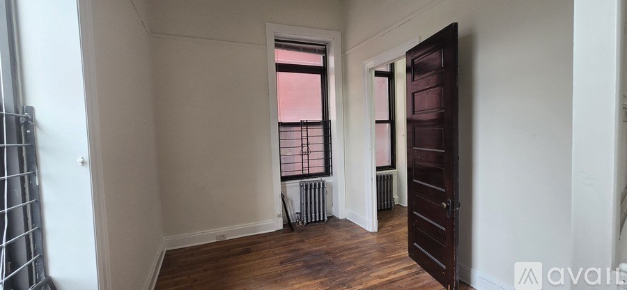 A room with a wooden floor and white walls, with a window that has a pink sky in the background.