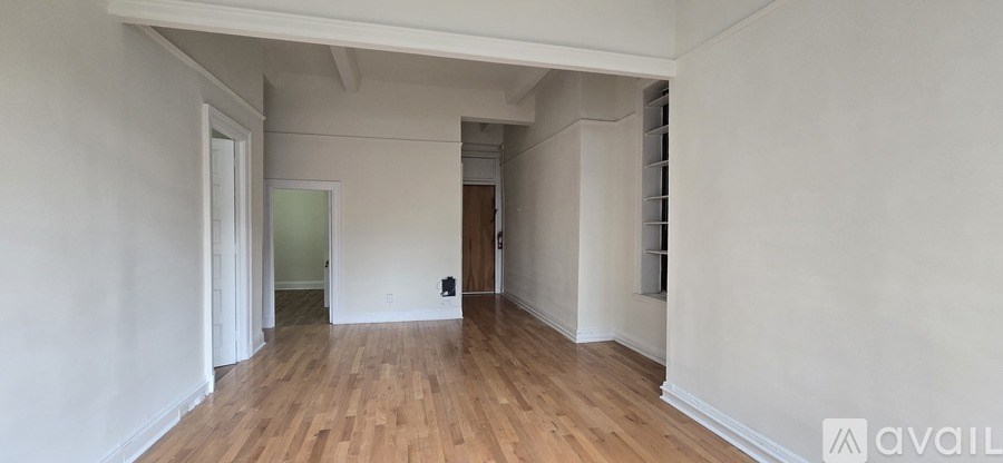 A room with wooden floors and white walls, with a door on the right and a window on the left.