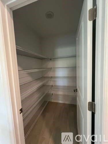 A white door with a handle is open to a hallway with a white ceiling and shelves.