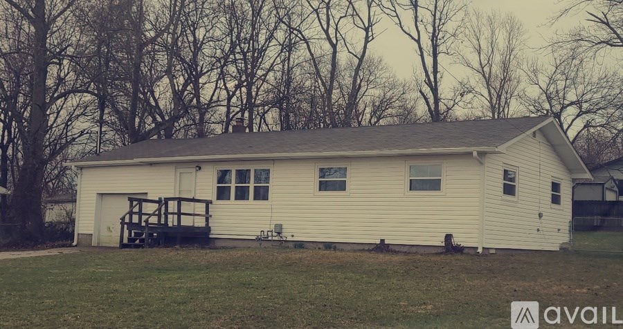 A white house with a porch and a tree in the background.