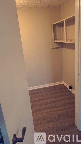 A room with a wooden floor and a white wall with a shelf on it.