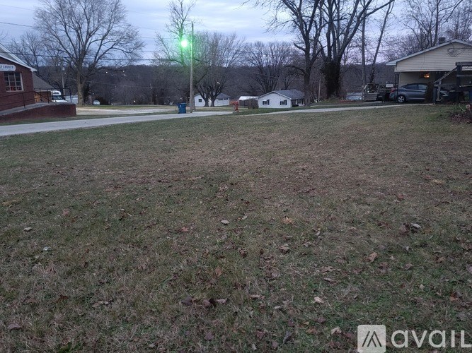 A grassy field with a house and trees in the background.