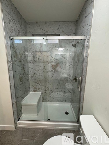 A white toilet is in a marble-tiled shower stall.