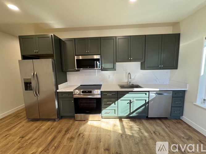A kitchen with dark green cabinets and a stainless steel refrigerator.