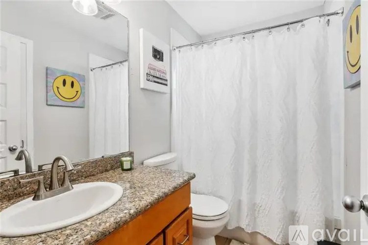 A bathroom with a white shower curtain and a smiley face picture on the wall.