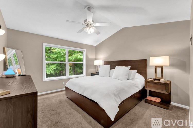 A bedroom with a large bed, a ceiling fan, and a window with a view of trees.