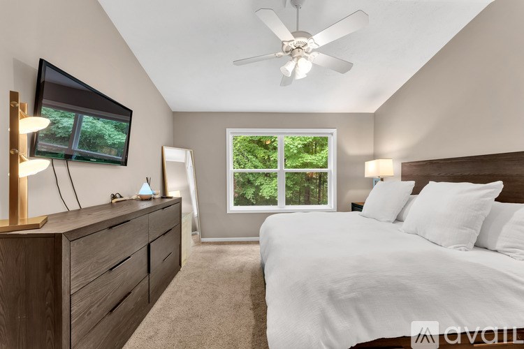 A bedroom with a large bed, a television, and a window with a view of trees.