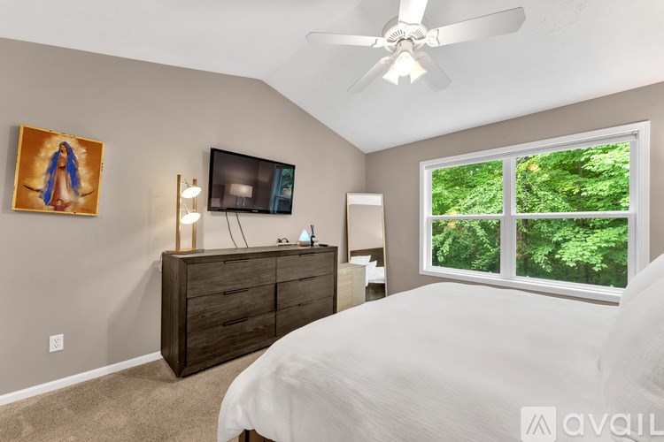 A bedroom with a bed, dresser, and a window showing greenery outside.