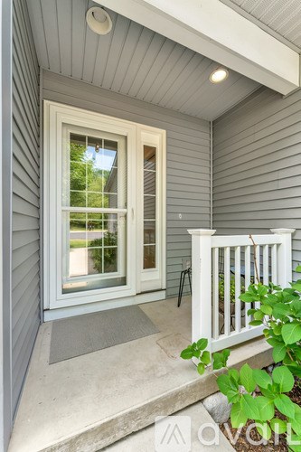 A white door with a glass window is on a porch with a white railing.