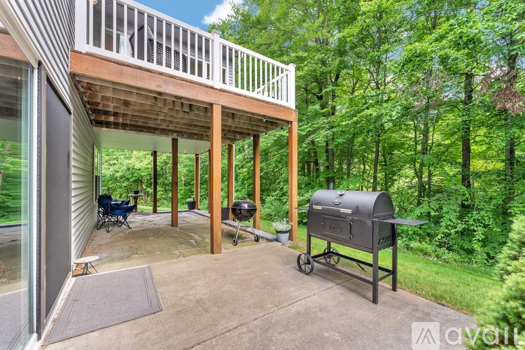 A patio with a grill and a chair is surrounded by trees.