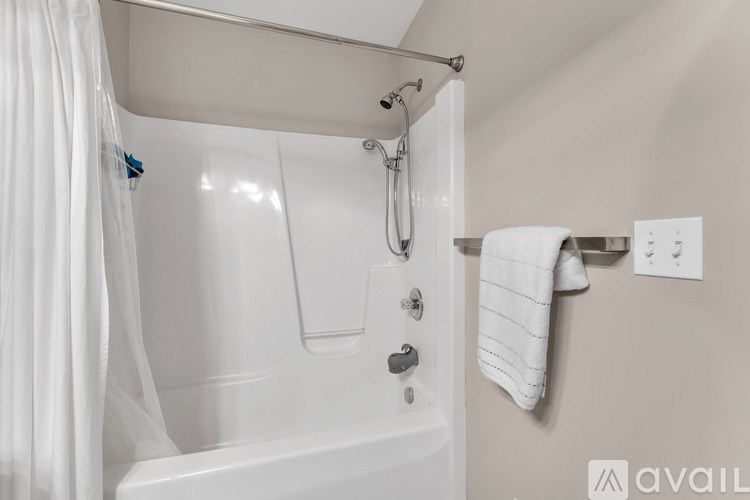 A white bathtub with a shower head and a towel hanging on the wall.