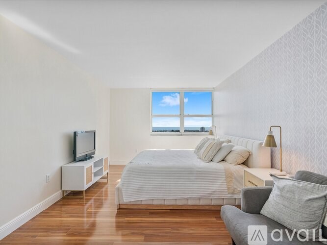 A bedroom with a large bed, a television, and a window overlooking the ocean.