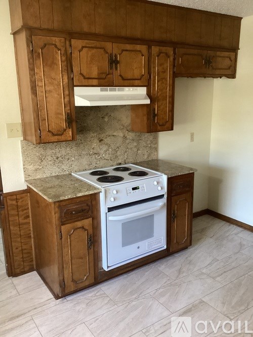 A kitchen with a white stove top oven and wooden cabinets.