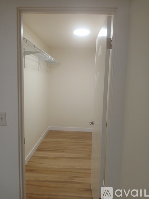A small room with a wooden floor and a white wall with a light switch.